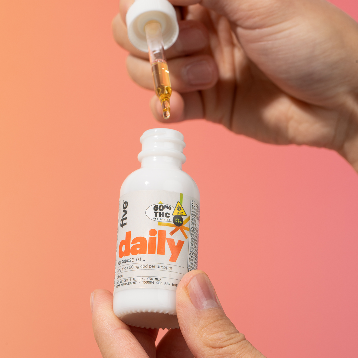 Hand holding dropper above white bottle labeled daily microdose oil; label shows '60MG THC' and '21+'.