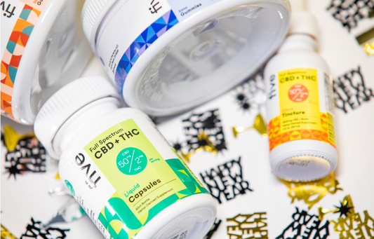 Bottles of CBD products labeled 'Full Spectrum CBD + THC', '50 mg CBD', '2 mg THC', 'Liquid Capsules', and 'Tincture' on a surface decorated with 'Happy New Year' confetti.