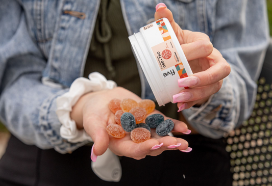 Person holding a container labeled 'Full Spectrum CBD + THC 25 mg per gummy Five Dual Spectrum Gummies' with orange and black gummies in the other hand.