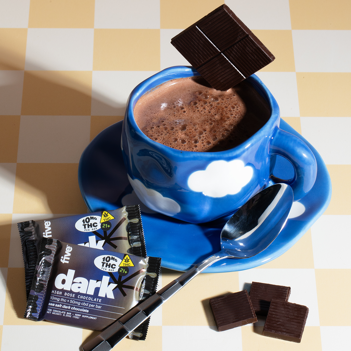 A cup of hot chocolate with a spoon and chocolate bars.
