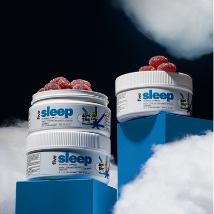 Two containers of sleep CBD gummies are stacked on blue platforms among fluffy white clouds. The containers have white lids and labels indicating 40 mg THC per serving, with red gummies visible on top of the stack. The background is dark.